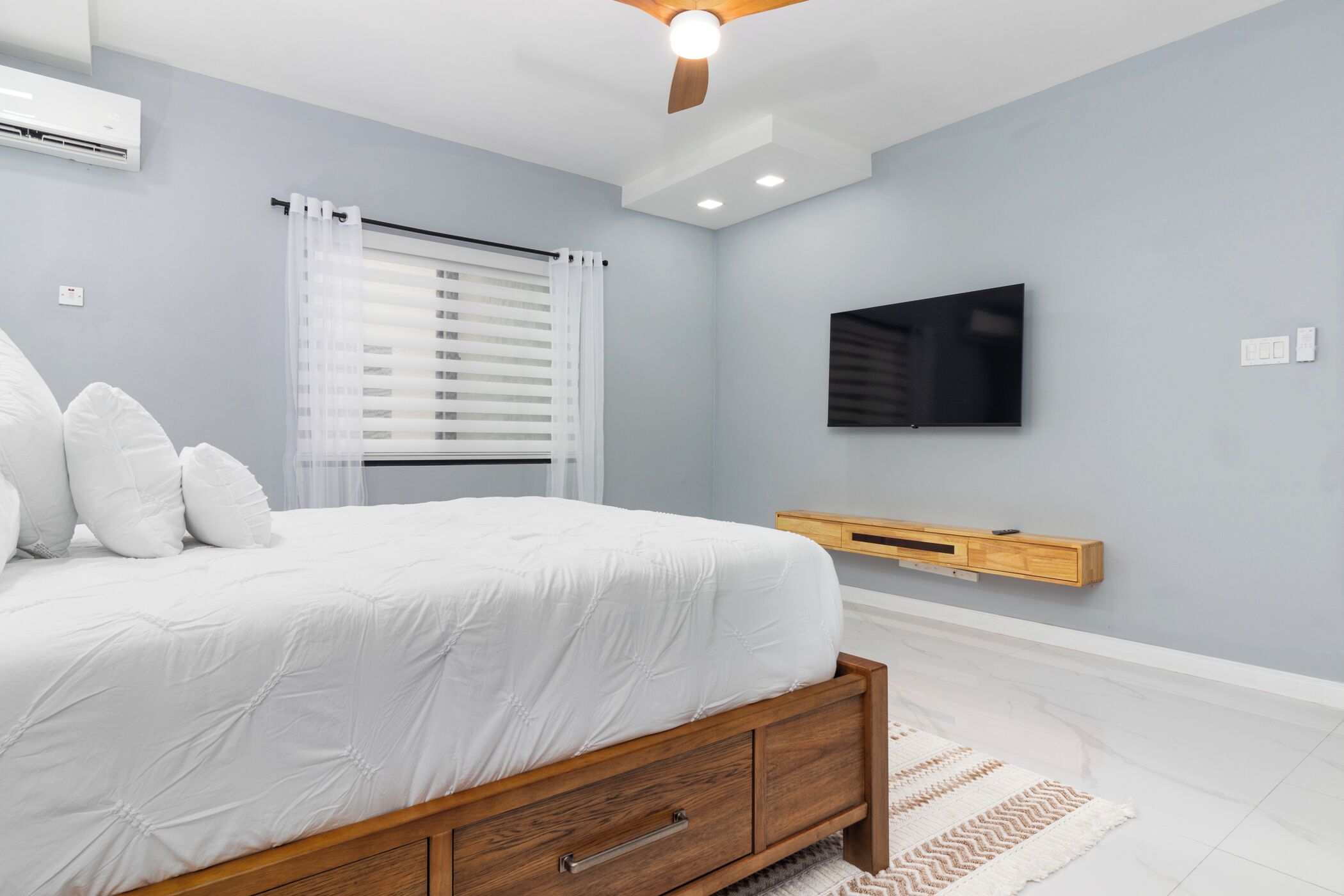 A bedroom with a bed, a TV mounted on the wall, and a ceiling fan.