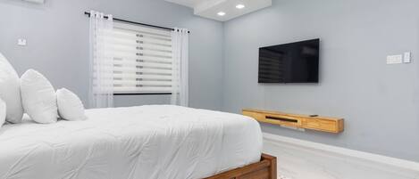 A bedroom with a bed, a TV mounted on the wall, and a ceiling fan.