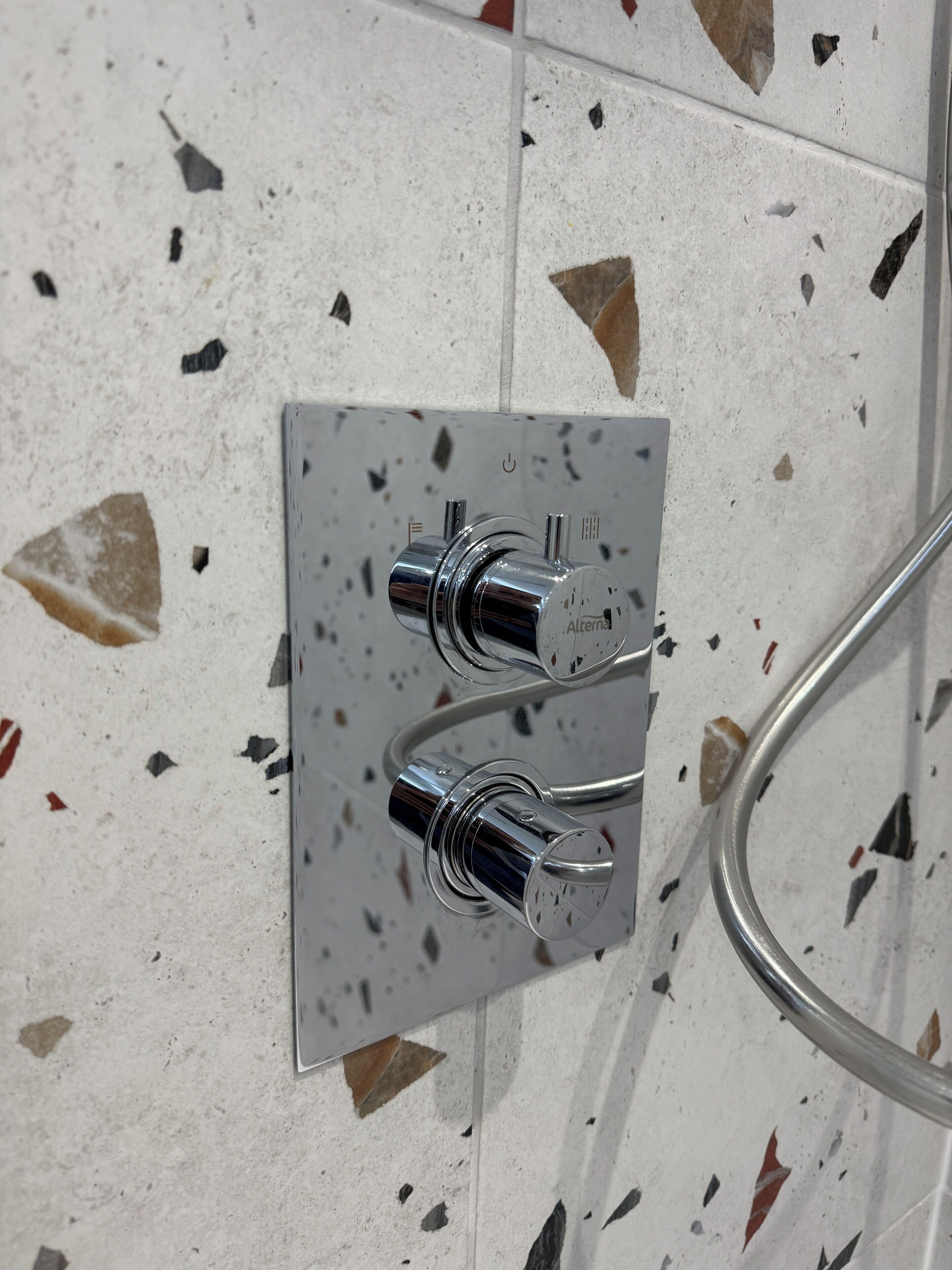 A bathroom with a chrome shower control panel and a glass shower enclosure.