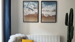 Ett rum med en vit soffa, en blå stol, en kaktus och två inramade tavlor på väggen.