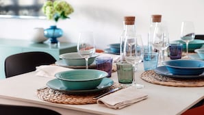A dining table set with blue and green plates, clear glasses, and a woven placemat. - Como Hills (Como)