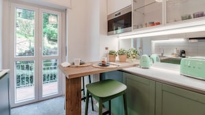 A modern kitchen with a wooden island, green bar stool, and a view through large windows. - Como Hills (Como)
