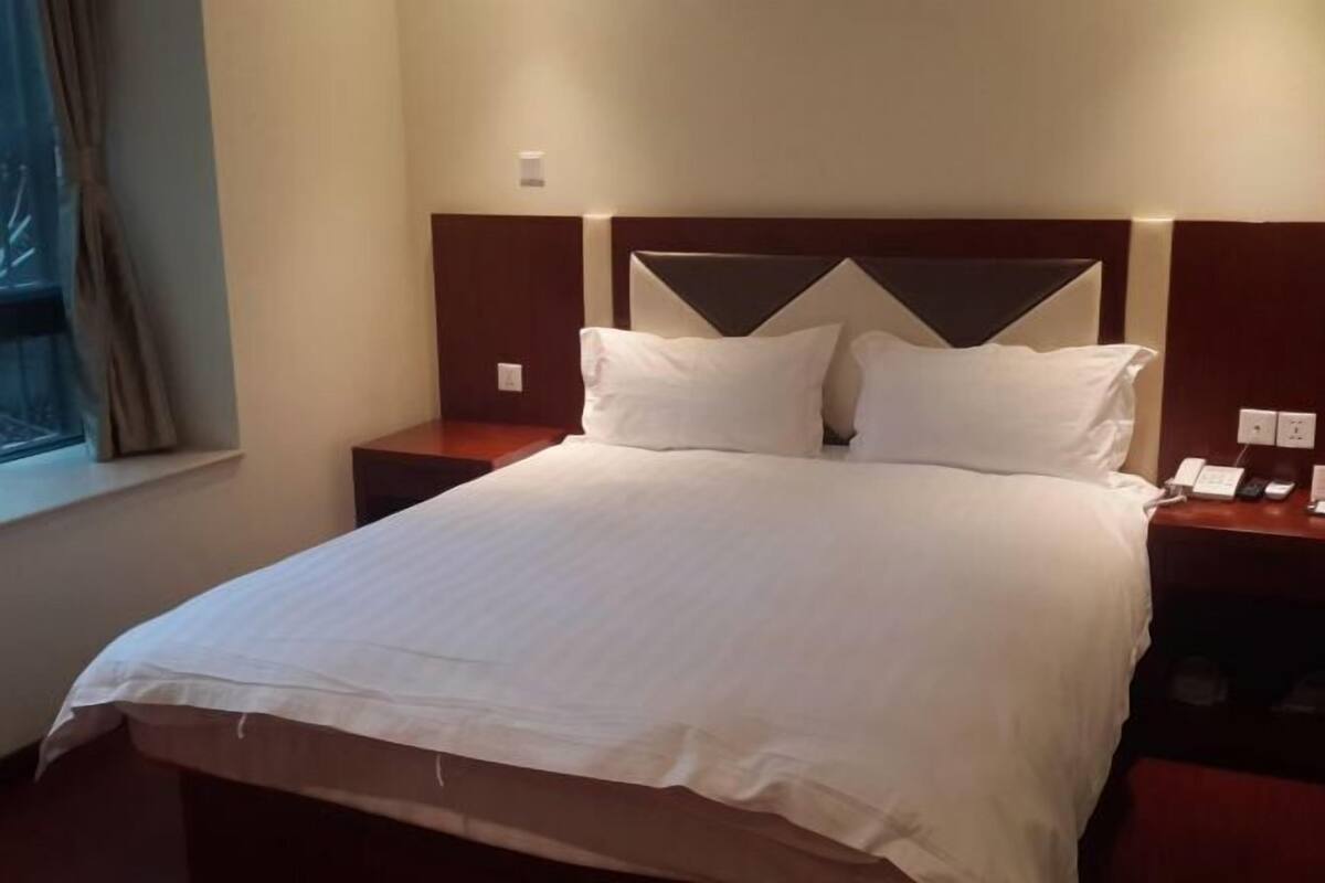 A hotel room with a large bed, a wooden headboard, two bedside tables with lamps, and a window with curtains.