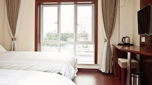 A hotel room with two beds, a desk, a TV, and a window with curtains.