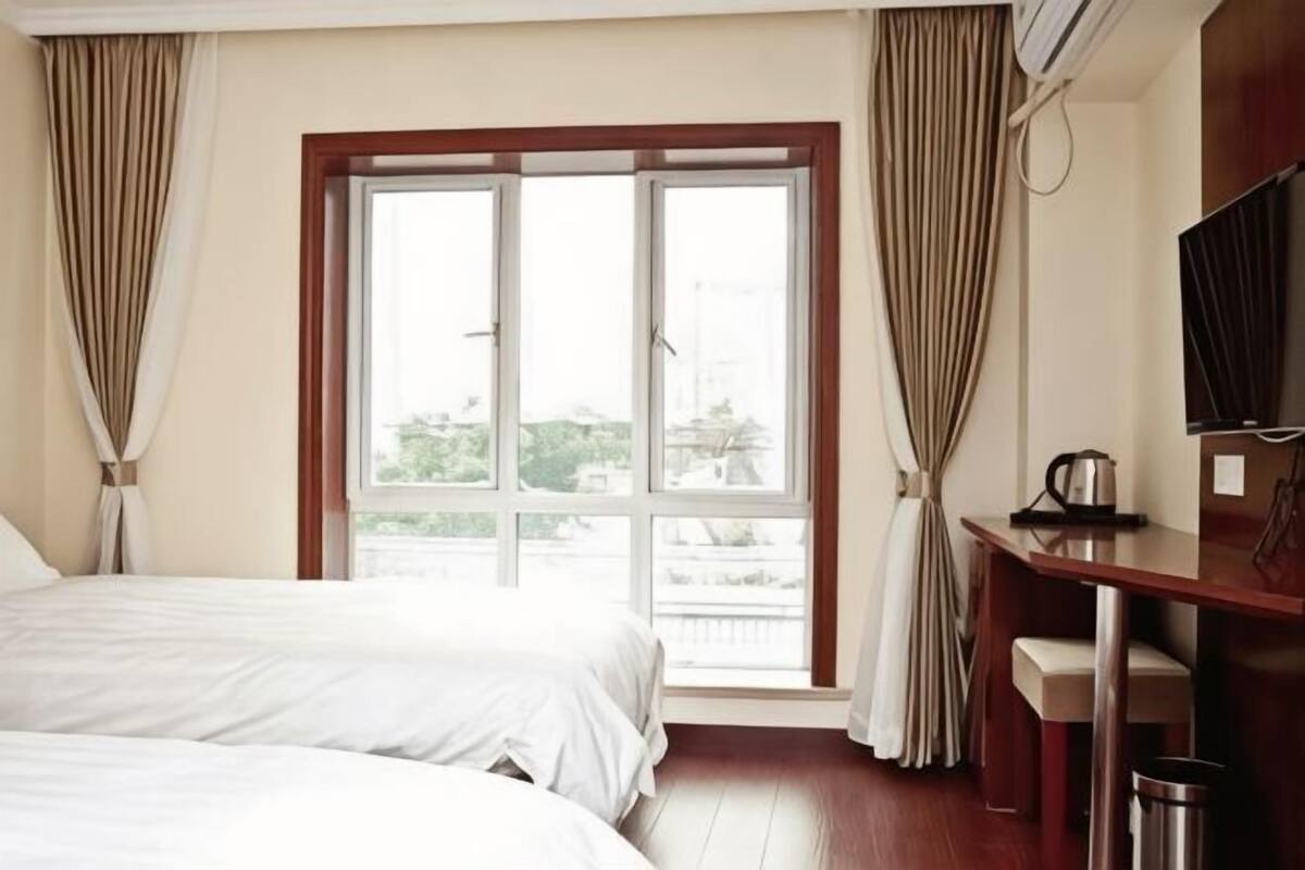 A hotel room with two beds, a desk, a TV, and a window with curtains.