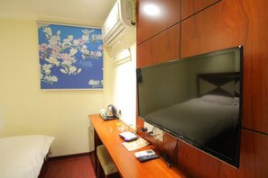 A hotel room with a wooden desk, a flat-screen TV, a bed, and a wall-mounted air conditioner. - Yanrui Hotel (Shanghai)