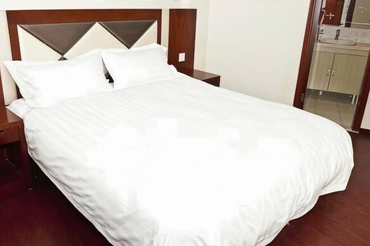 A neatly made bed with a wooden headboard, a bedside table, and a mirror.