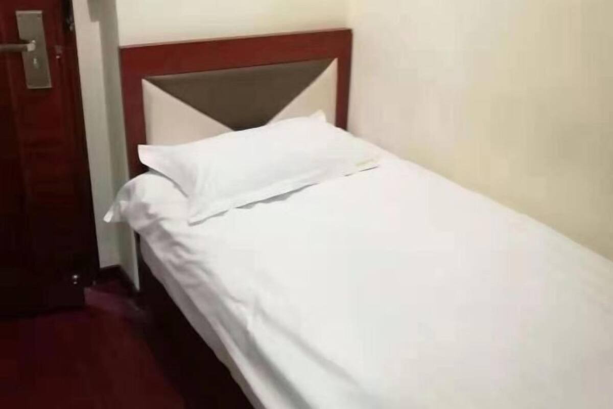 A single bed with white bedding in a room with a wooden headboard and a door to the left.