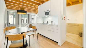 A modern kitchen with white cabinets, a microwave, and a sink. There is a dining area with a round table and chairs.