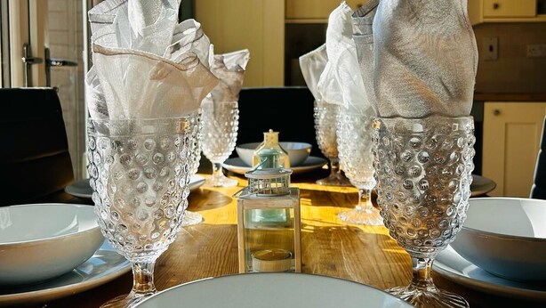 A dining table set with clear glassware and white plates, with a lantern in the center. - Beautiful, fully equipped, pet friendly 3 bedroom house in Shakespeare County. (Alcester)