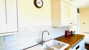 A kitchen with white cabinets, a wooden countertop, a sink, and a wall clock. - Beautiful, fully equipped, pet friendly 3 bedroom house in Shakespeare County. (Alcester)