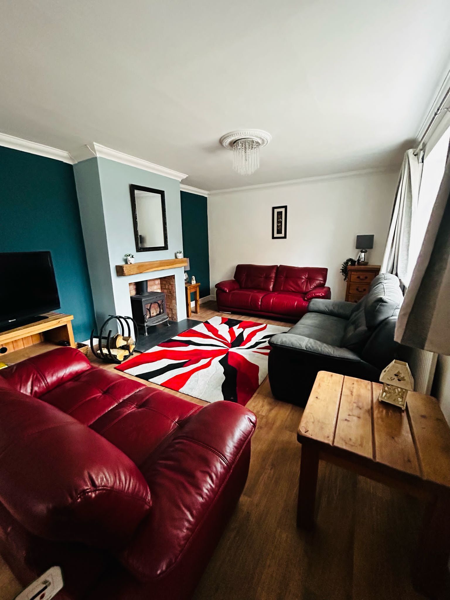 A living room with a fireplace, red leather sofas, a wooden coffee table, and a large rug.
