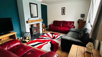 A living room with a fireplace, red leather sofas, a wooden coffee table, and a large rug.