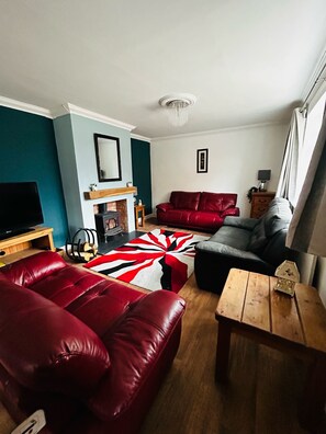 A living room with a fireplace, red leather sofas, a wooden coffee table, and a large rug. - Beautiful, fully equipped, pet friendly 3 bedroom house in Shakespeare County. (Alcester)