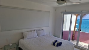 A bedroom with a bed, a ceiling fan, a nightstand, and a view of the ocean through a sliding door. - Very spacious and incredible views (Puerto Morelos)