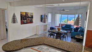 A modern kitchen with a granite countertop, a dining area with a round table and chairs, a blue sofa, and a view of the ocean through large windows. - Very spacious and incredible views (Puerto Morelos)