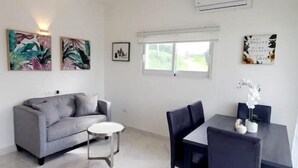 A modern living room with a grey sofa, a round coffee table, and a dining table with chairs. There are two wall-mounted paintings and a framed picture. - A luxurious and peaceful place with AC, free WIFI, private patio, and balcony! (Sosúa)