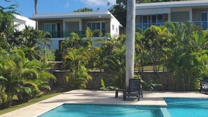 A swimming pool with a lounge chair, surrounded by palm trees and a building with large windows. - A luxurious and peaceful place with AC, free WIFI, private patio, and balcony! (Sosúa)