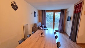 A spacious room with a wooden dining table, chairs, a sofa, and a balcony with curtains. - 200m from ski slopes, floor -1, terrace, tv, ski locker, 45m², Valfréjus (Valfréjus)