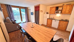 A compact living space with a dining table, chairs, a sofa, a kitchen area with wooden cabinets and appliances, and a sliding glass door leading to an outdoor area. - 200m from ski slopes, floor -1, terrace, tv, ski locker, 45m², Valfréjus (Valfréjus)