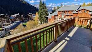 Un balcon doté d’une balustrade en bois, donnant sur une région montagneuse parsemée de bâtiments.