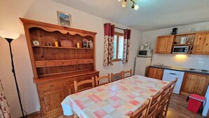 Une cuisine chaleureuse avec des meubles en bois, une table à manger recouverte d’une nappe à carreaux et un four à micro-ondes.