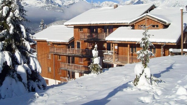 Un chalet en bois doté de plusieurs balcons, entouré d’arbres couverts de neige et avec des montagnes en arrière-plan.