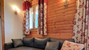 Un salon moderne avec un canapé d’angle, des murs recouverts de panneaux en bois et des rideaux à motifs floraux.