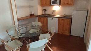 A compact kitchen with wooden cabinets, a microwave, a refrigerator, and a glass dining table with chairs.