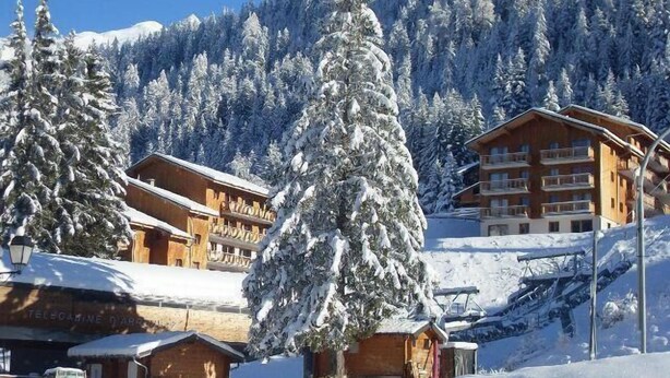 A snow-covered mountain resort with wooden buildings, including a lodge and a multi-story hotel.