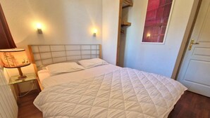 A neatly made bed with a quilted white duvet, a bedside lamp with a deer design, and a wooden headboard.