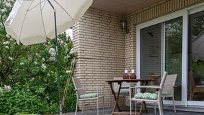 Un patio con una mesa, sillas, un paraguas blanco y una pared de ladrillo.