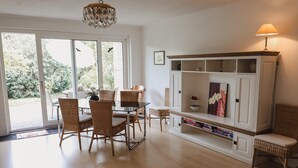 Un salón espacioso con zona de comedor, ventanas amplias, una araña y un mueble blanco para entretenimiento.