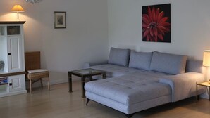 Una sala moderna con un sofá gris, una mesita, un sillón de mimbre y un armario.