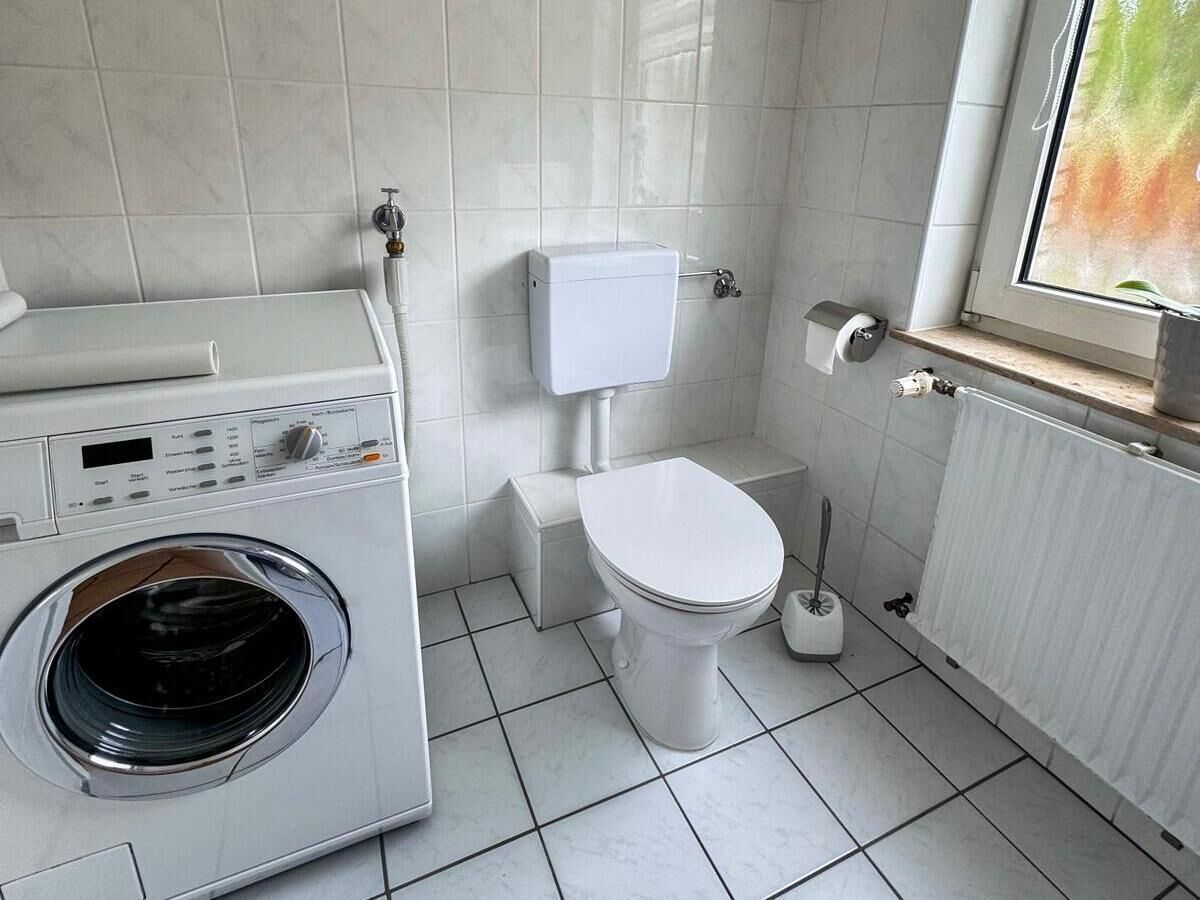 A compact laundry room with a washing machine, toilet, and radiator.