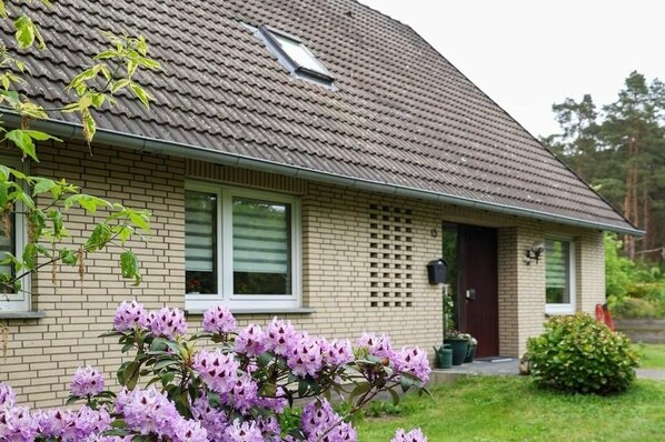 Une maison avec un toit en pente, une façade en briques et un petit porche à l’avant.