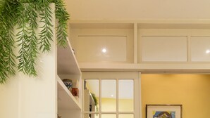 Ein Zimmer mit einer weißen Tür, einem Bücherregal mit Büchern und Dekoration, einem gerahmten Bild an der Wand und einem gefliesten Boden.