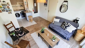 A compact living space with a dining area, a sofa, a coffee table, and a small kitchen area with a washing machine. - Le Salluste: T2 cosy with balcony in Strasbourg. (Strasbourg)