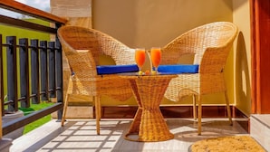 Un balcon avec des meubles en osier, deux verres de jus d’orange et une plante en pot.