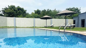 Une piscine avec un revêtement de sol en carrelage, deux chaises longues et un parasol.