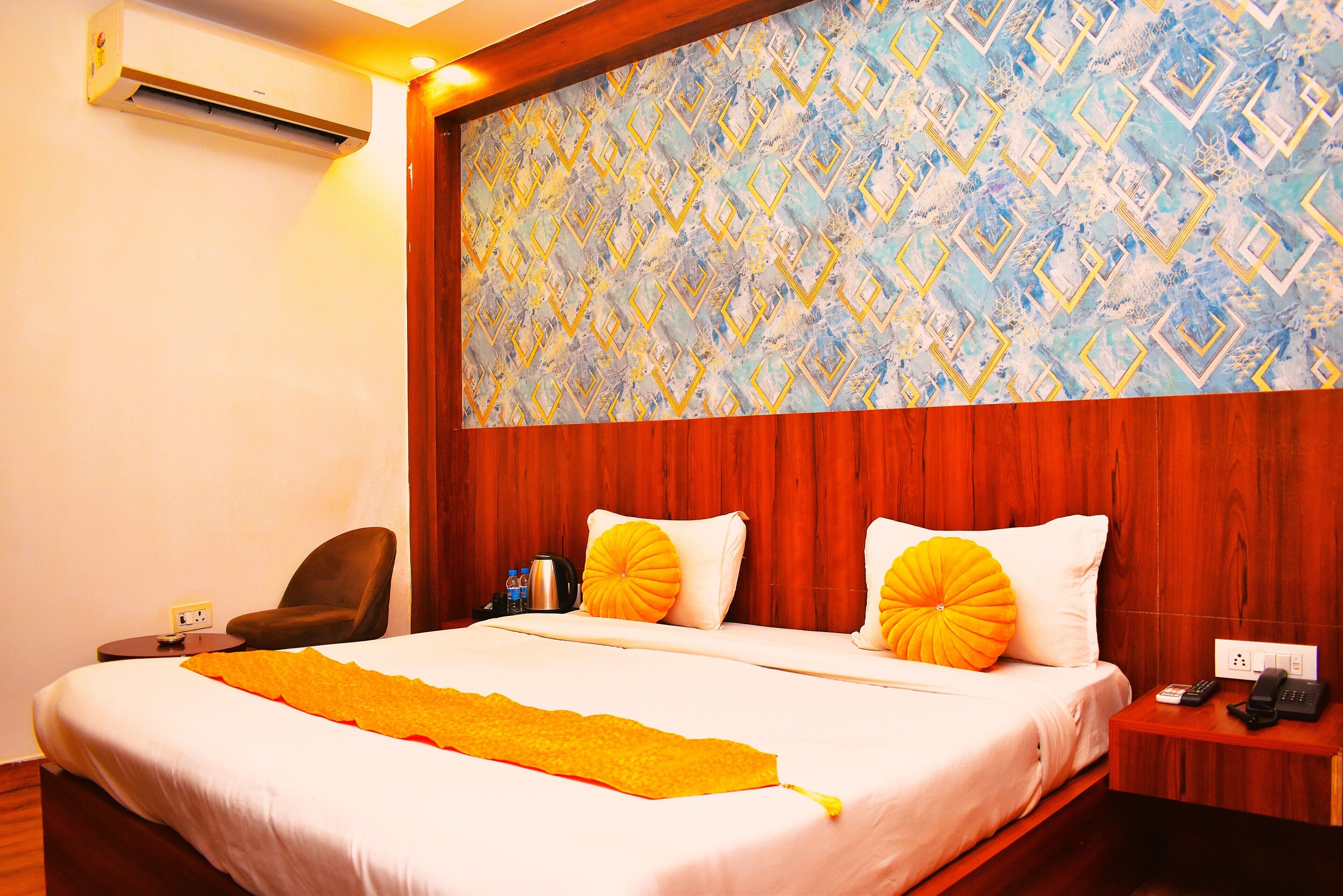 A hotel room with a bed, a wooden headboard, a nightstand, a chair, and an air conditioning unit.