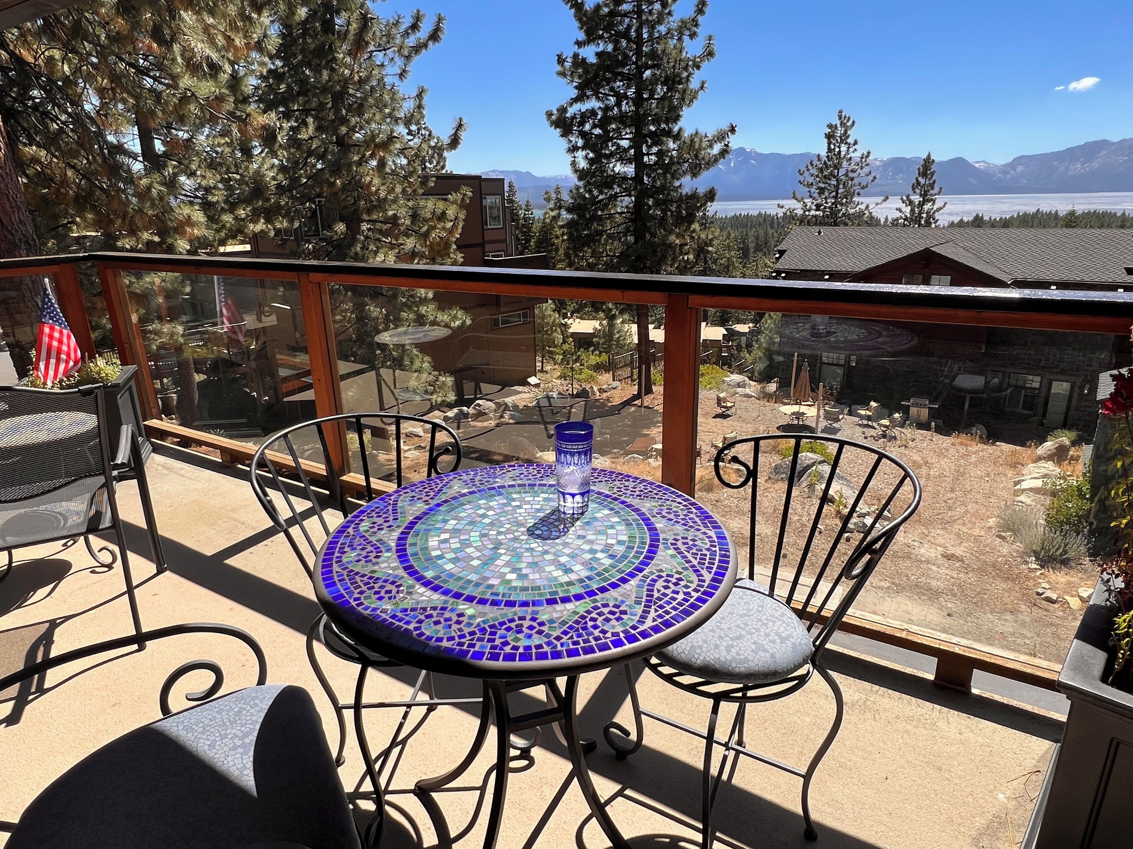 Uma varanda com mesa e cadeiras de mosaico, com vista para uma paisagem montanhosa e um corpo de água.