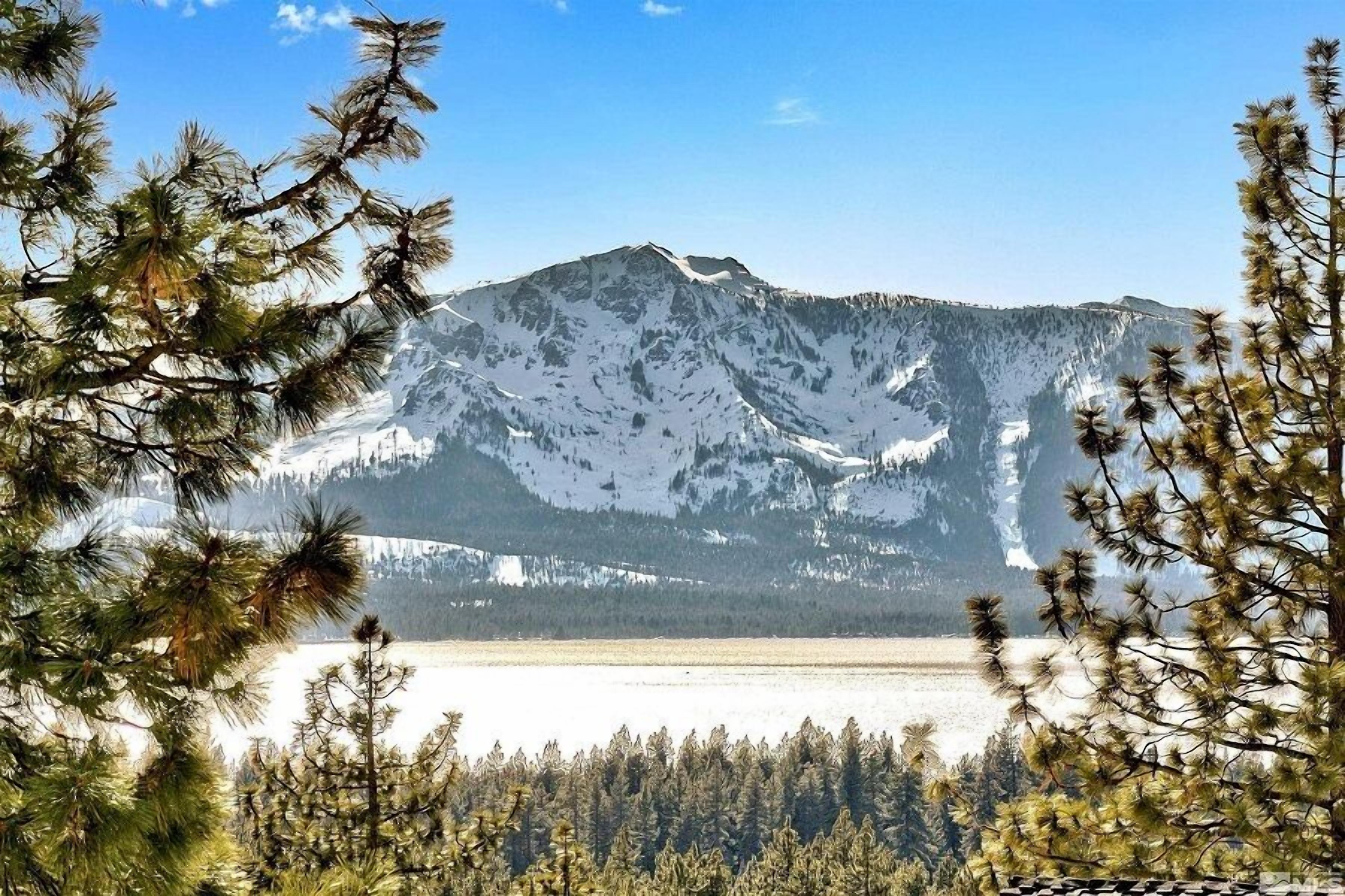 Una montaña con picos nevados y un lago al frente.