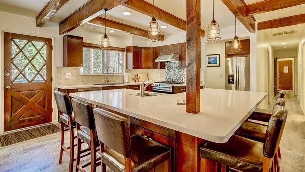 A spacious kitchen with a large island, wooden beams, and pendant lighting.