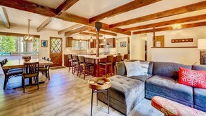 A spacious living area with a wooden ceiling, a dining table with chairs, and a sofa with a red pillow.