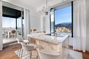 Una cocina moderna con encimera de mármol, taburetes de bar, una araña y vistas de la ciudad a través de amplios ventanales.