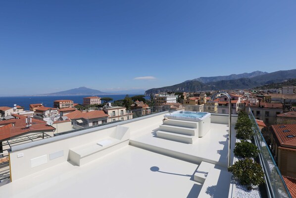 A rooftop terrace with a pool, overlooking a coastal town and mountains.