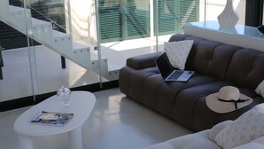 A modern living room with a glass staircase, a brown leather sofa with a laptop and a hat, and a white coffee table with a magazine. - The Square in Sorrento (Sorrento)