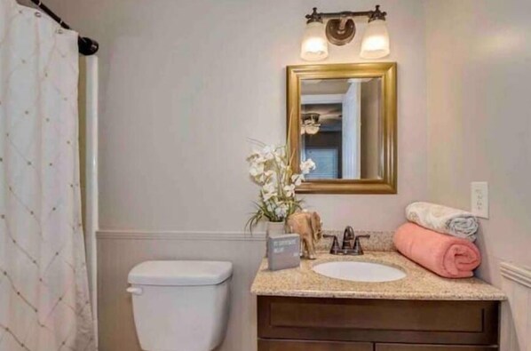 Een badkamer met een wit toilet, een wastafel met een roze handdoek en een spiegel met een gouden lijst.