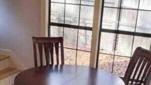 Un comedor con una mesa redonda y cuatro sillas, ventanas amplias y piso de baldosas.